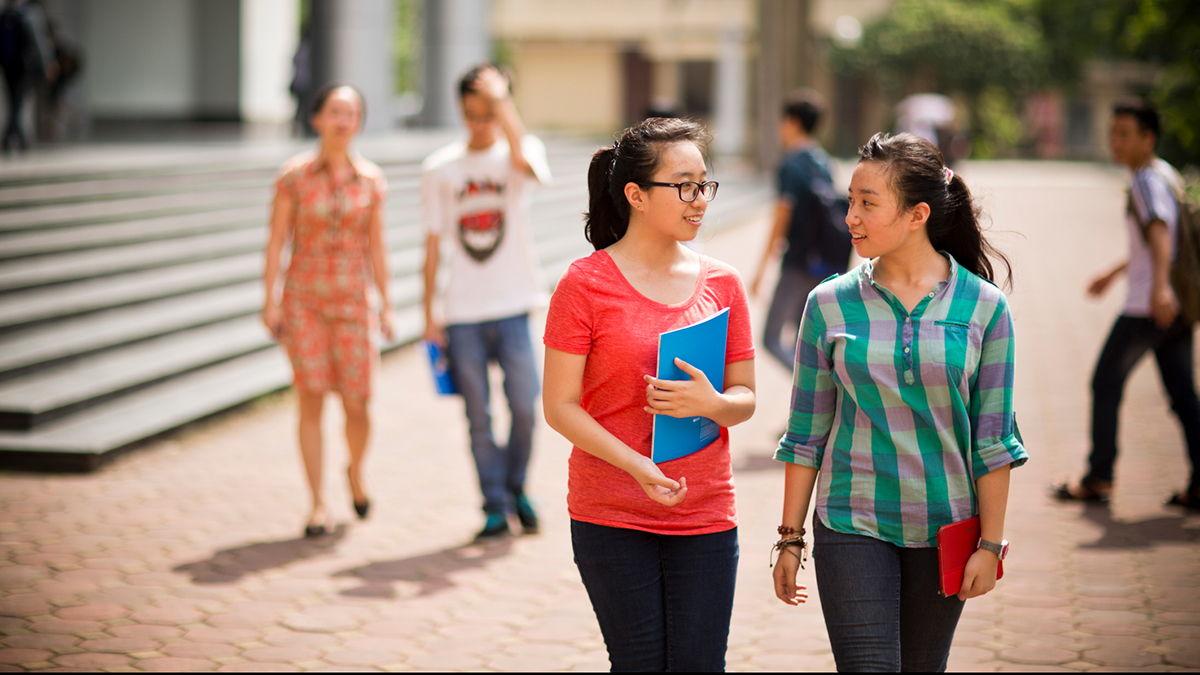 Two Vietnamese women talking to each other whilst walking on the street.