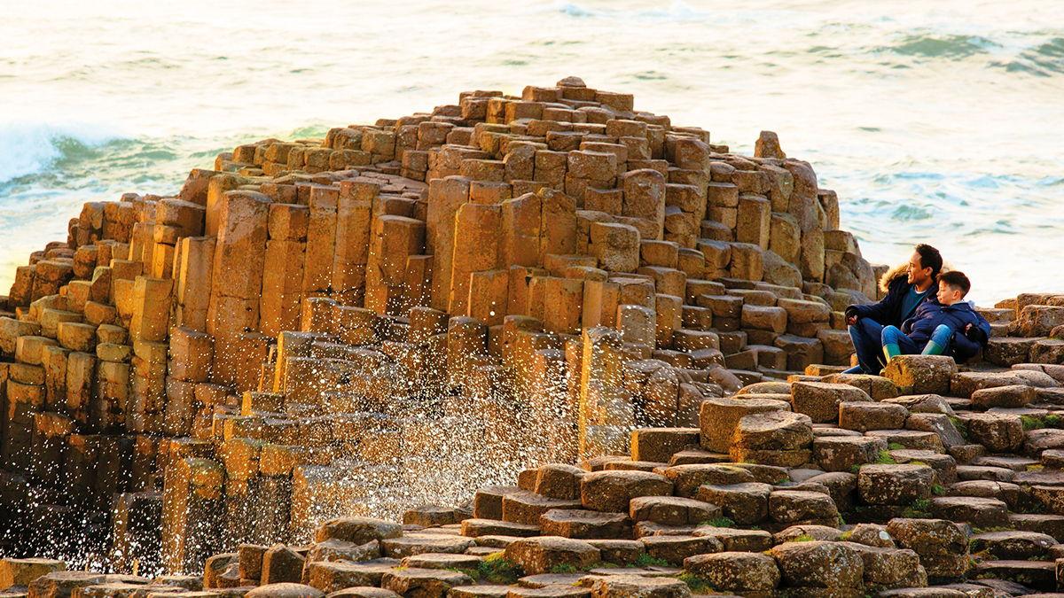 Man and boy sitting on the red basalt columns of The Giant's Causeway, County Antrim, Northern Ireland.