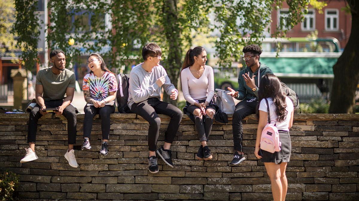Multi-racial young people sitting on a brick fence chatting with each other.